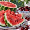 Картина диня и череши: нарязана диня, купа череши и раирана покривка пред градина, маслен стил